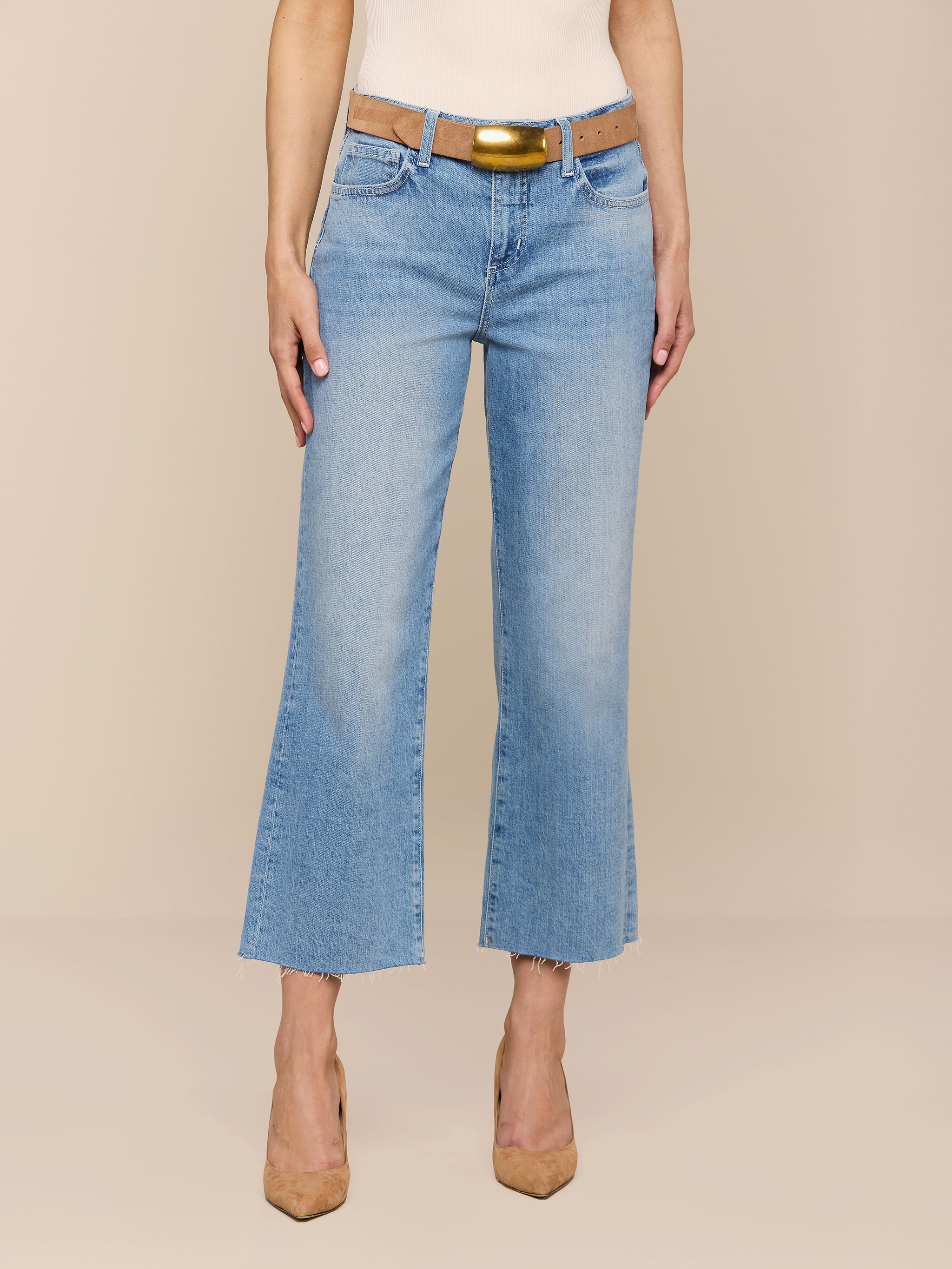 A person wearing the Wanda Cropped Wide-Leg Jean in a light blue wash, styled with a brown belt and tan heels, standing against a plain white background.