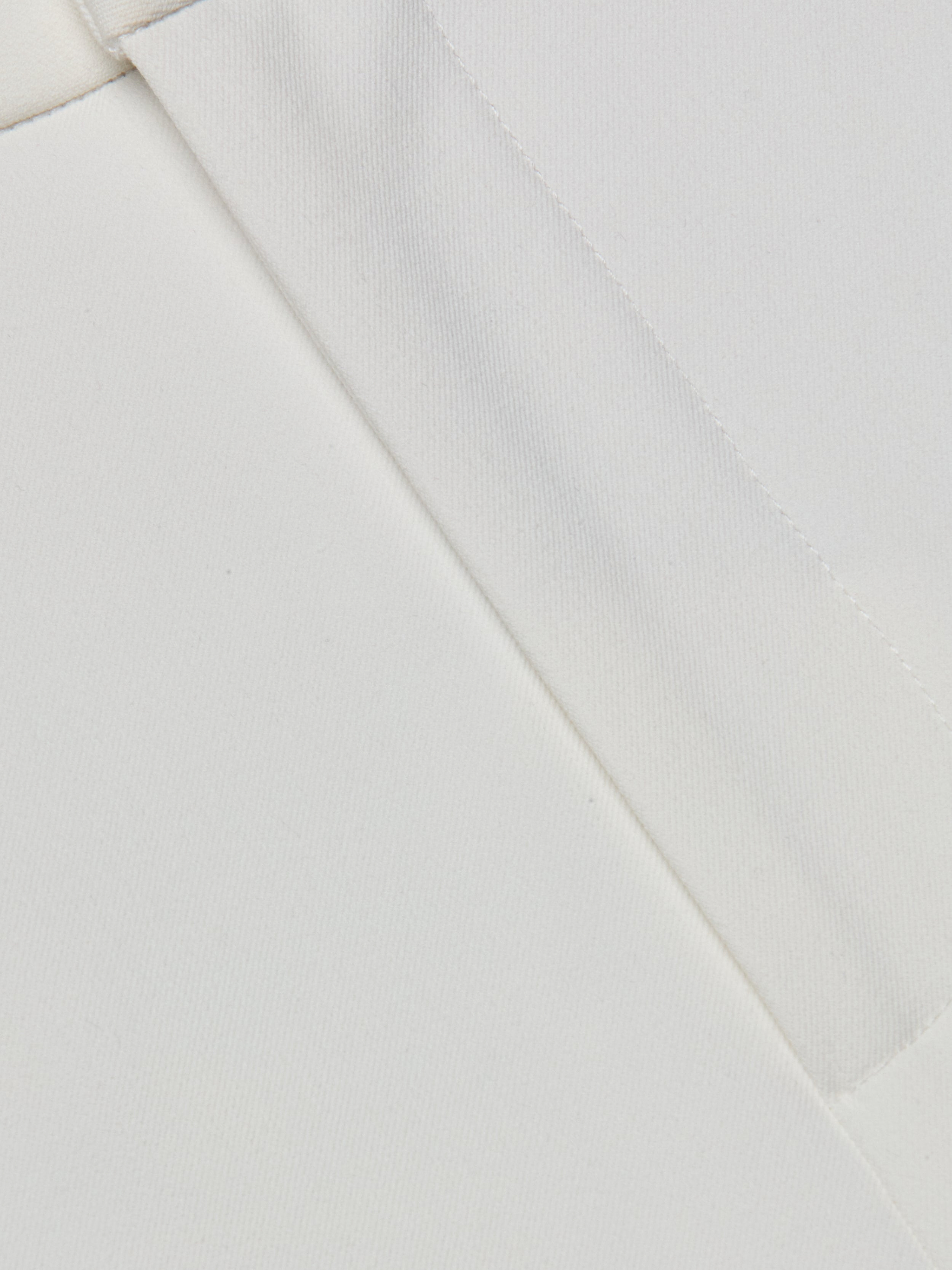 Close-up of the Rebel Trouser white stretch fabric, featuring two seams intersecting at an angle to showcase the texture and detailed stitching.