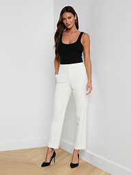 A woman stands with her hands in her pockets against a plain, light background, wearing a black sleeveless top, black heels, and the Rebel Trouser—high-rise white straight-leg trousers crafted from stretch suit fabric.