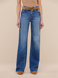 A person stands against a plain white background wearing the Clayton Wide-Leg Jean in high rise denim blue, crafted from REPREVE woven denim, styled with a brown belt and tan shoes. The upper body is cropped out of the image.