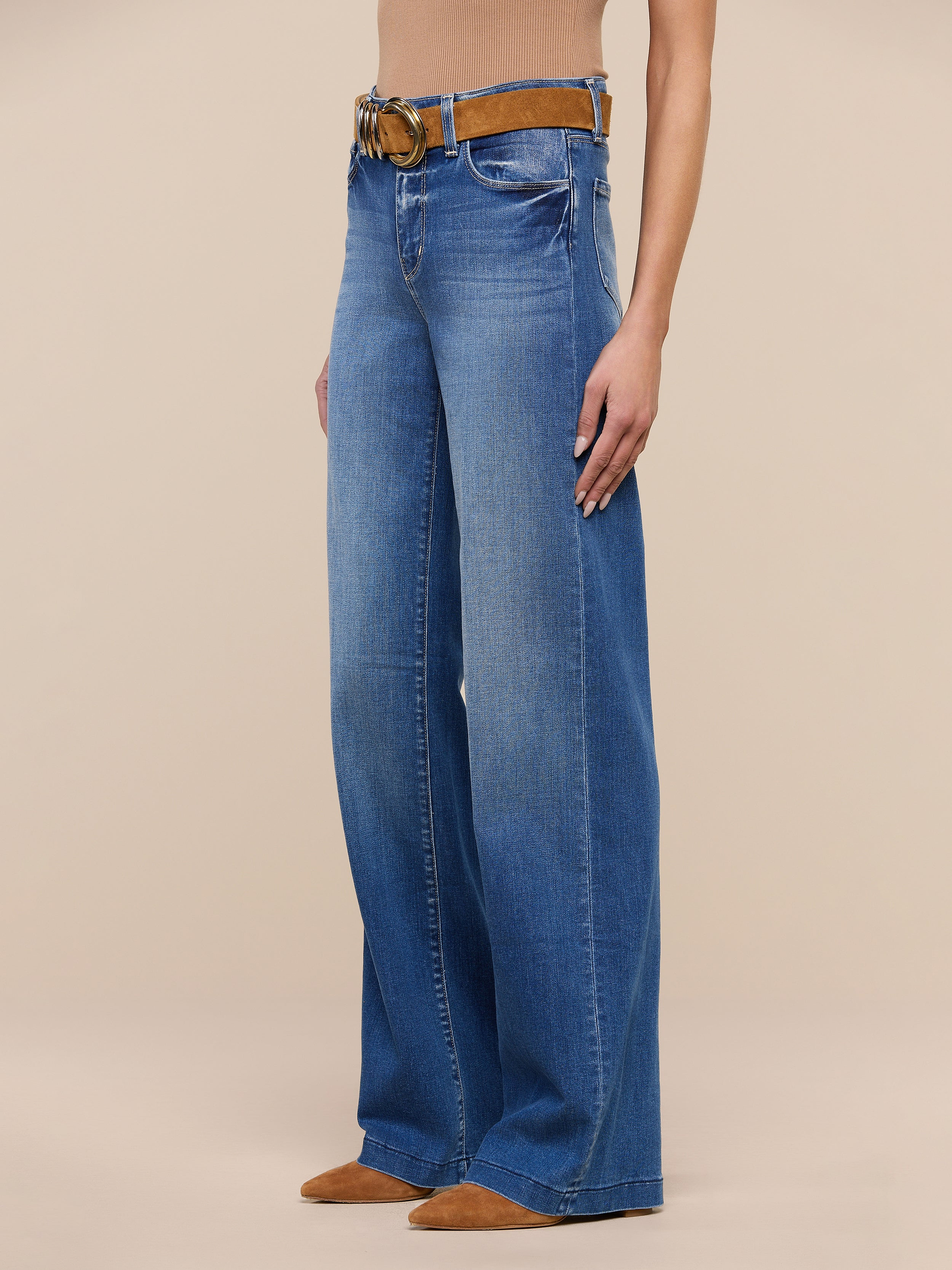 A person wearing the Clayton Wide-Leg Jean in blue high rise REPREVE woven denim, styled with a brown belt and brown pointed-toe shoes, stands against a plain white background. The upper body is mostly out of frame.