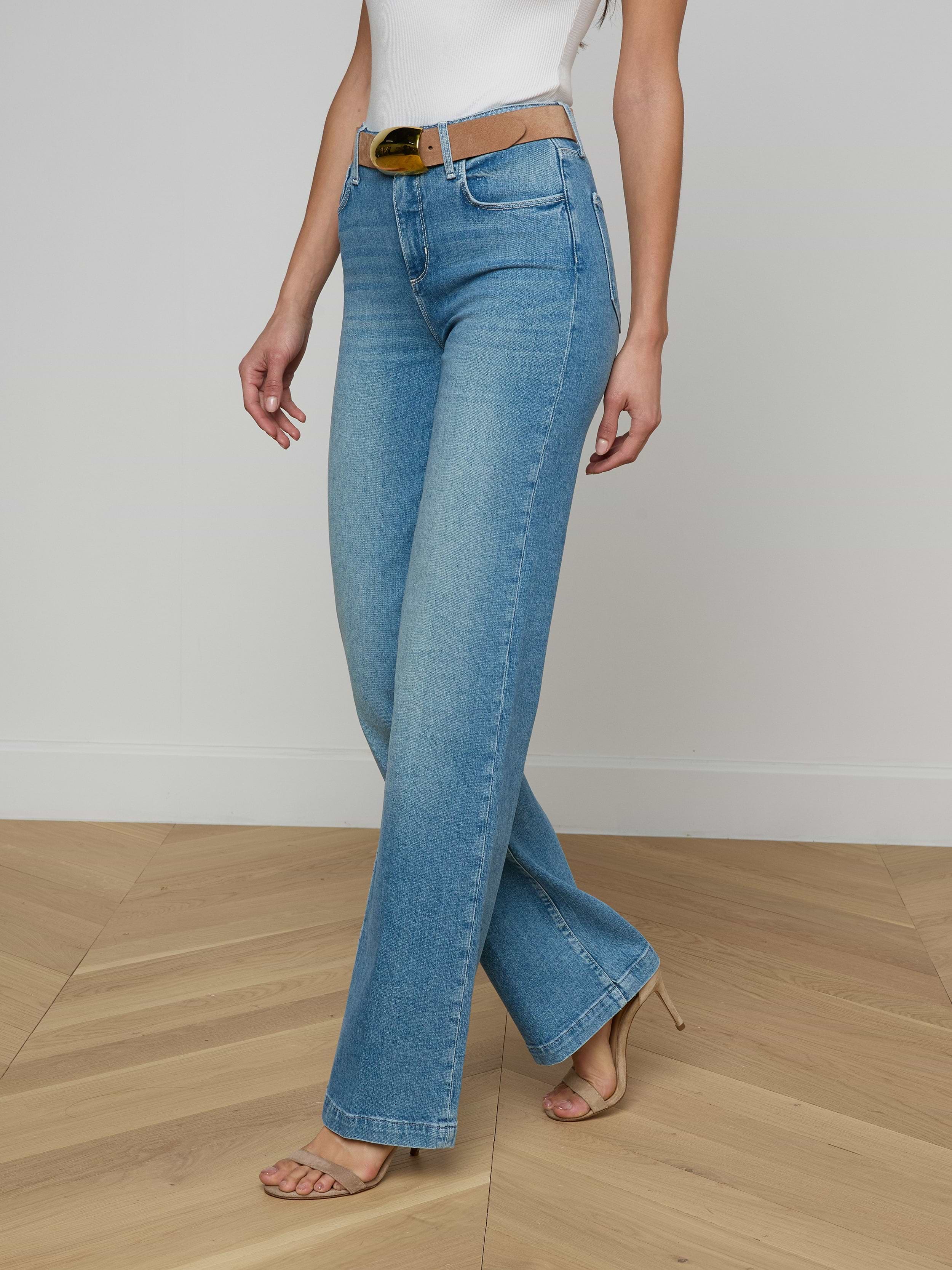 A person wearing the Clayton Wide-Leg Jean in light blue, paired with a white belt, a white sleeveless top, and open-toe heels stands against a plain white background.