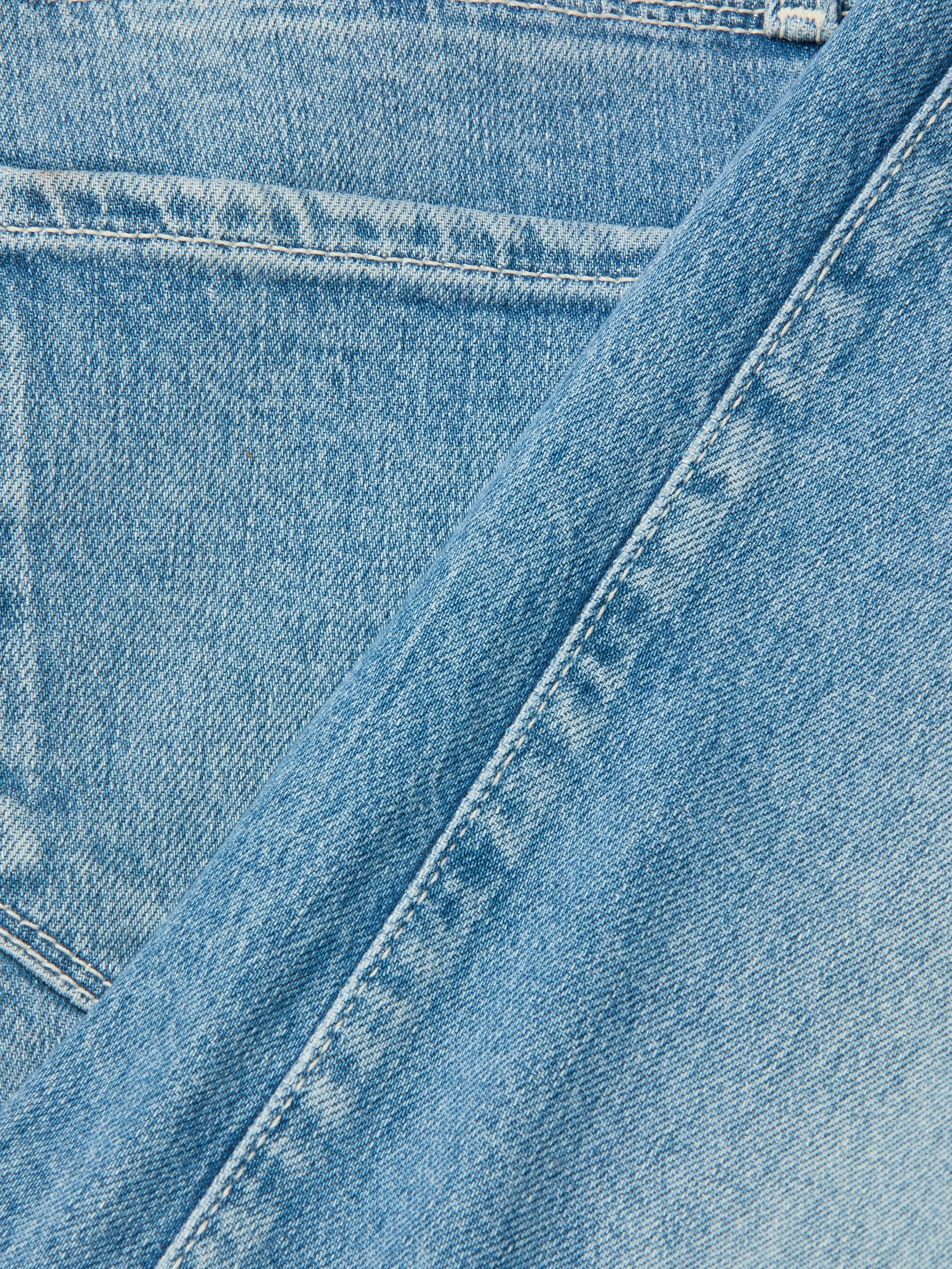 Close-up of light blue denim fabric with pocket and seam details, highlighting the texture and stitching characteristic of the Clayton Wide-Leg Jean.