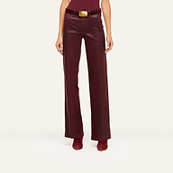A person wearing high-waisted burgundy leather pants, a burgundy top, matching boots, and a wide belt with a large gold buckle stands confidently against a plain white background.