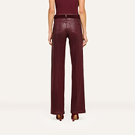 A person stands facing away, wearing the Clayton Coated Wide-Leg Jean featuring a contoured waistband in a rich burgundy hue, paired with a matching belt and heels. The background is plain and light-colored.