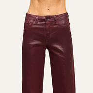 A person wearing high-waisted, shiny burgundy leather pants stands against a plain light background, with the image cropped to show only the waist and upper legs.