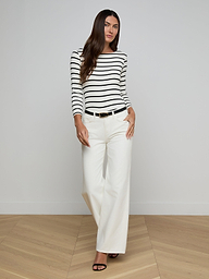 A woman stands against a plain background, wearing a black and white striped long-sleeve top, high rise Alicent Wide-Leg Jeans in white, a black belt, and black heels.