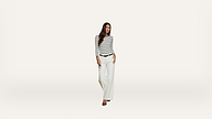 Woman wearing a black-and-white striped long-sleeve shirt, white wide-leg pants, and black heels stands against a plain white background.