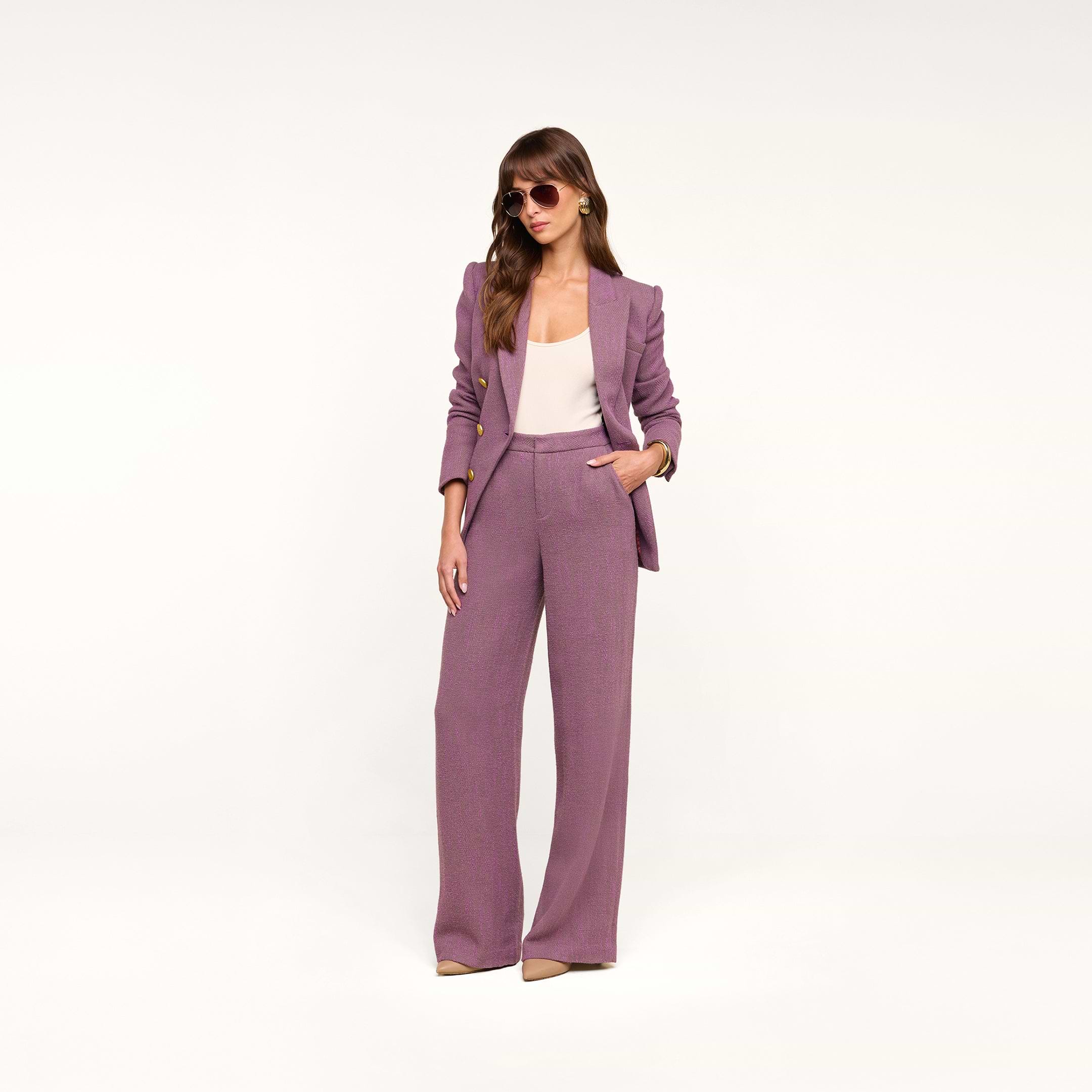 A woman stands confidently with one hand in her pocket against a plain, light background, wearing the Livvy Straight-Leg Trouser in mauve, paired with a white top, sunglasses, and beige heels.