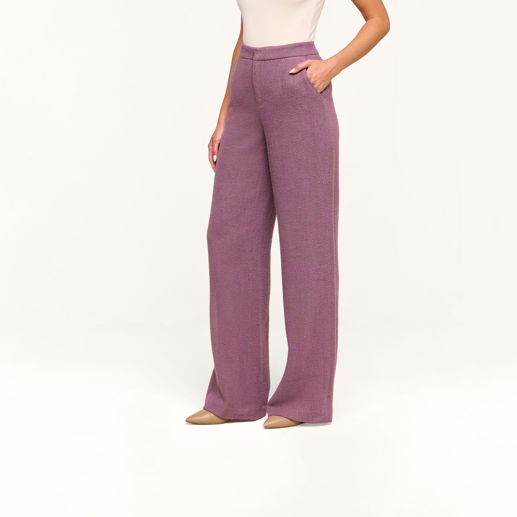 Woman wearing Livvy Straight-Leg Trouser in high rise purple herringbone with hands in pockets, paired with a sleeveless beige top and beige pointed-toe shoes, standing against a plain white background.