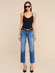 A woman in sunglasses, a black tank top, and the Nevia Slouchy Straight-Leg Jean—vintage-inspired, blue, ripped, and crafted from all-cotton denim—styled with a black belt and black heels stands against a plain white background.