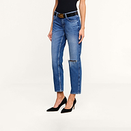 Woman wearing Nevia Slouchy Straight-Leg Jean, featuring vintage-inspired all-cotton denim in blue with a ripped knee, paired with a black belt, black sleeveless top, and black high heels, standing against a plain white background.