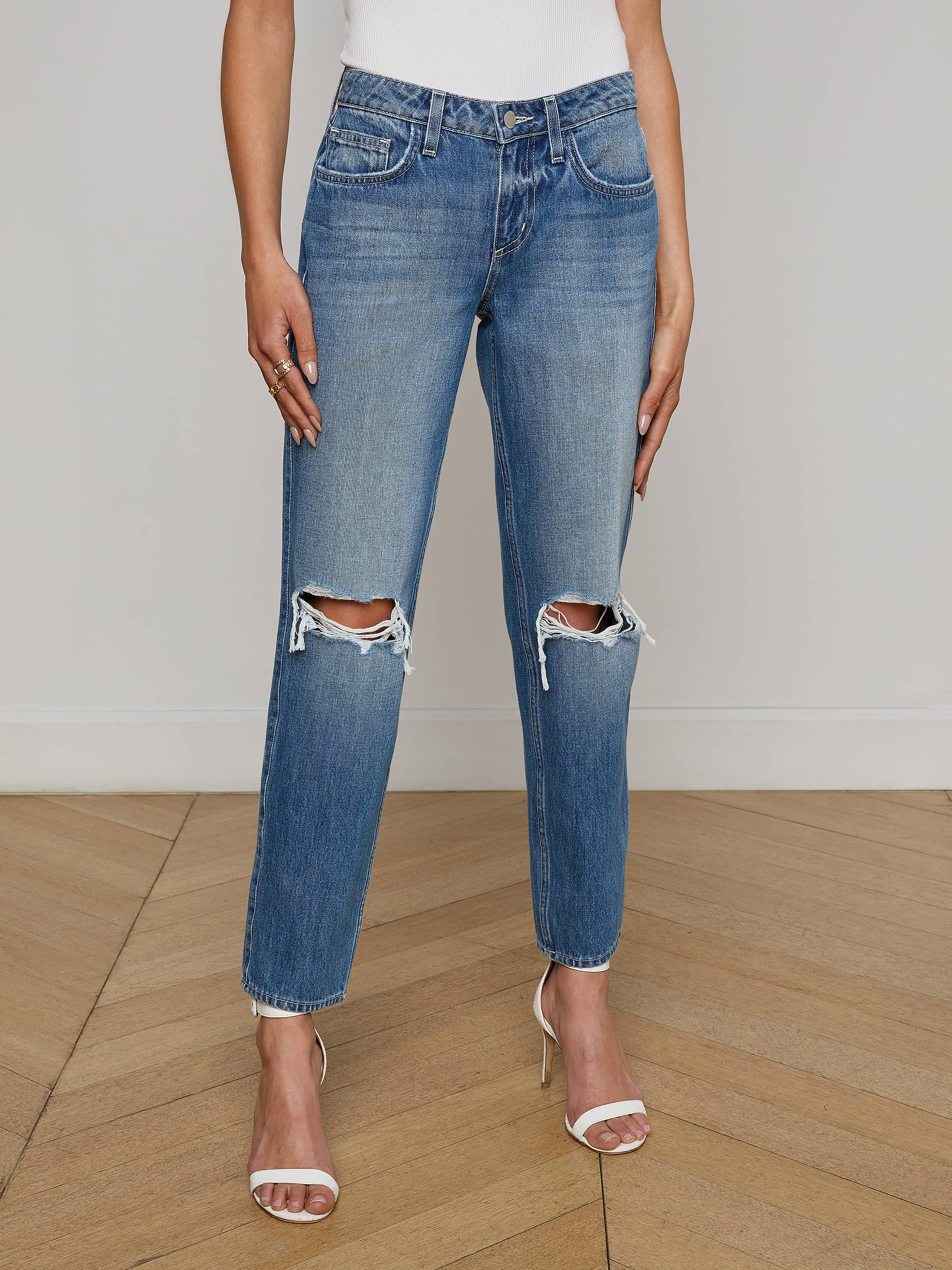 Wearing the Nevia Slouchy Straight-Leg Jean in a blue wash with ripped knees, paired with a white top and nude high-heeled sandals, this person stands against a plain white background.