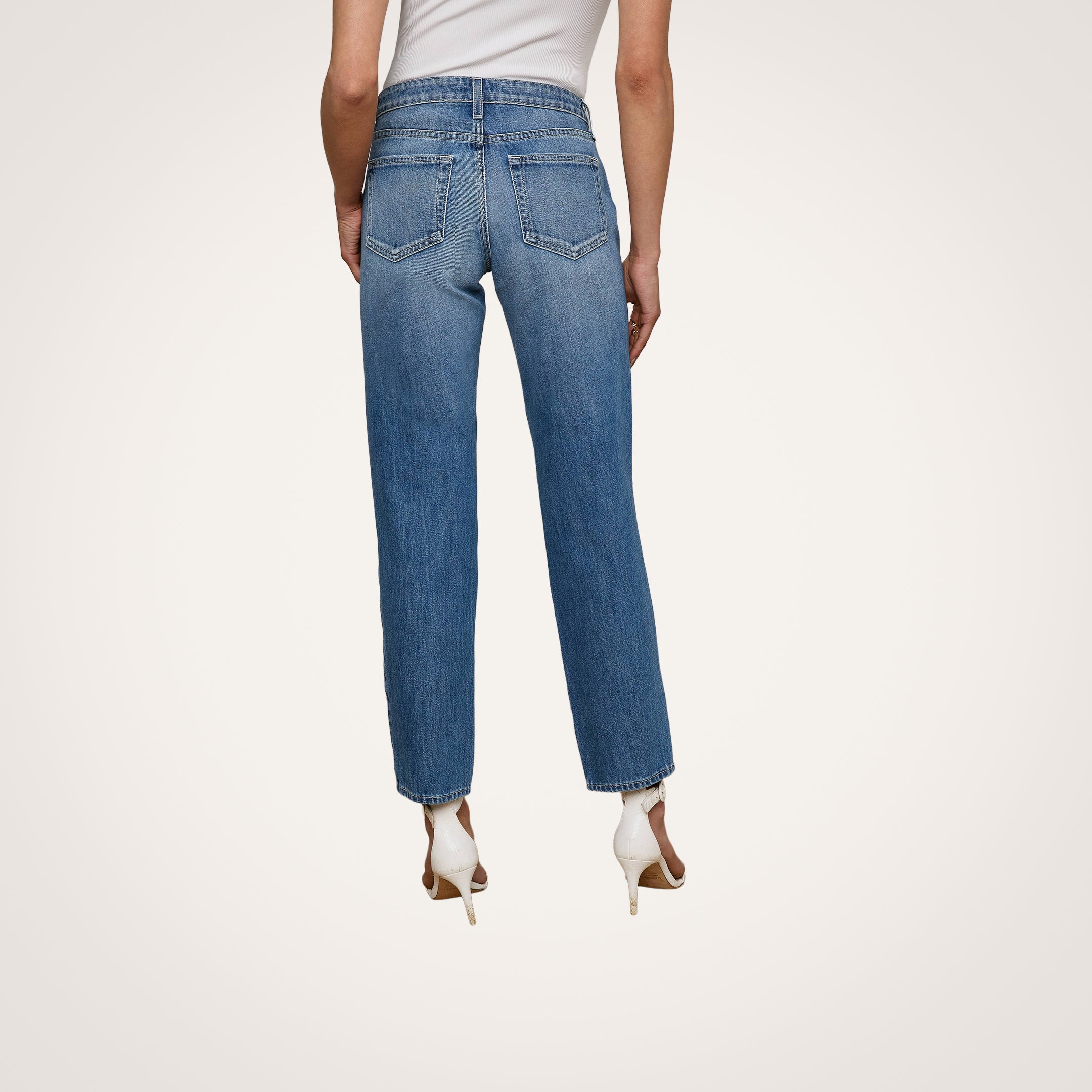 A person is seen from the back wearing the Nevia Slouchy Straight-Leg Jean in a blue wash, paired with white high-heeled shoes. The jeans feature back pockets and visible stitching, set against a plain, light-colored background.