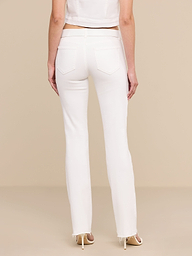 A woman stands facing away, wearing the Sneeki Low-Rise Straight-Leg Jean in white with a raw hem, paired with a white cropped top and beige heels against a plain white background.