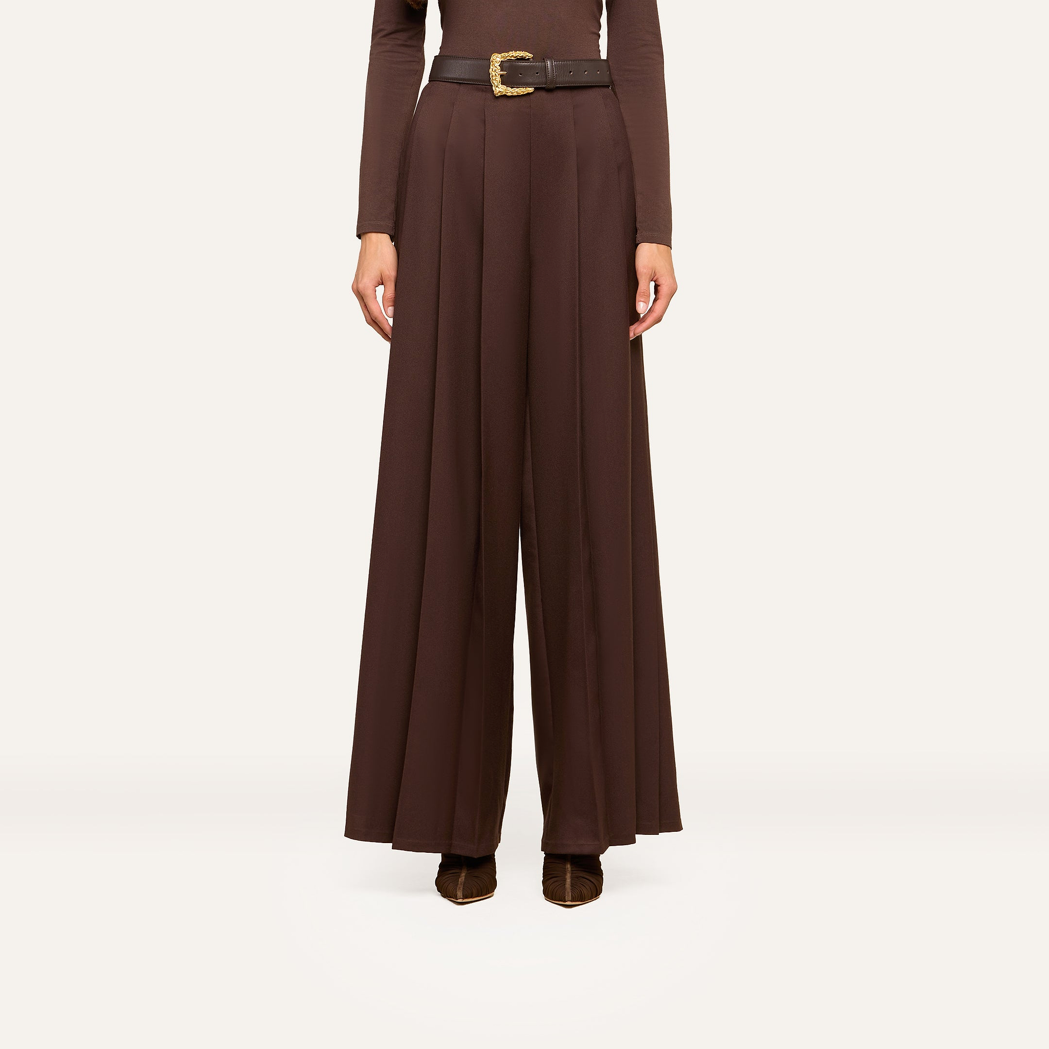 A person wearing high-waisted, wide-leg brown trousers with a black belt and brown shoes, shown from shoulders down against a plain white background, exudes effortless style.