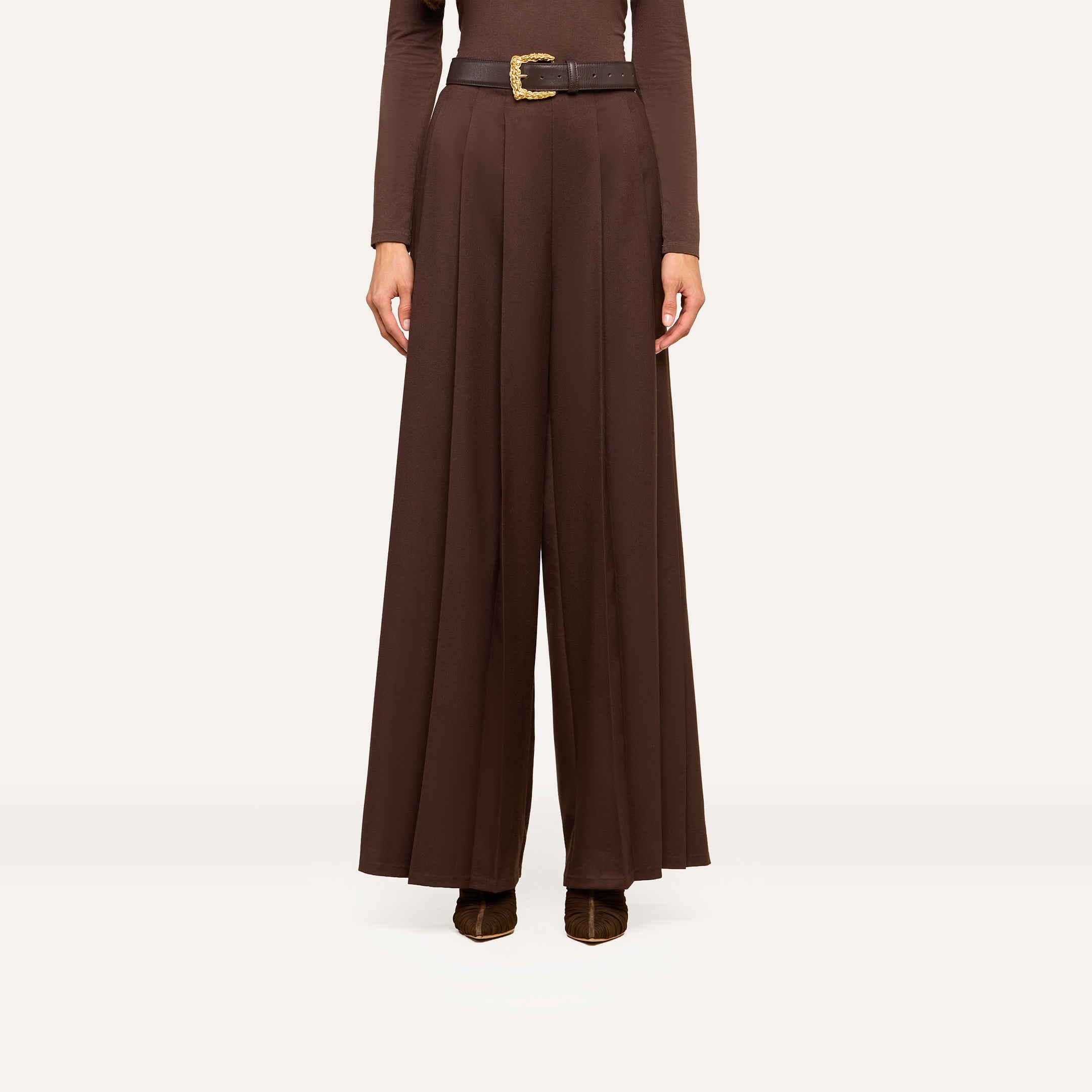 A person wearing high-waisted, wide-leg brown trousers with a black belt and brown shoes, shown from shoulders down against a plain white background, exudes effortless style.