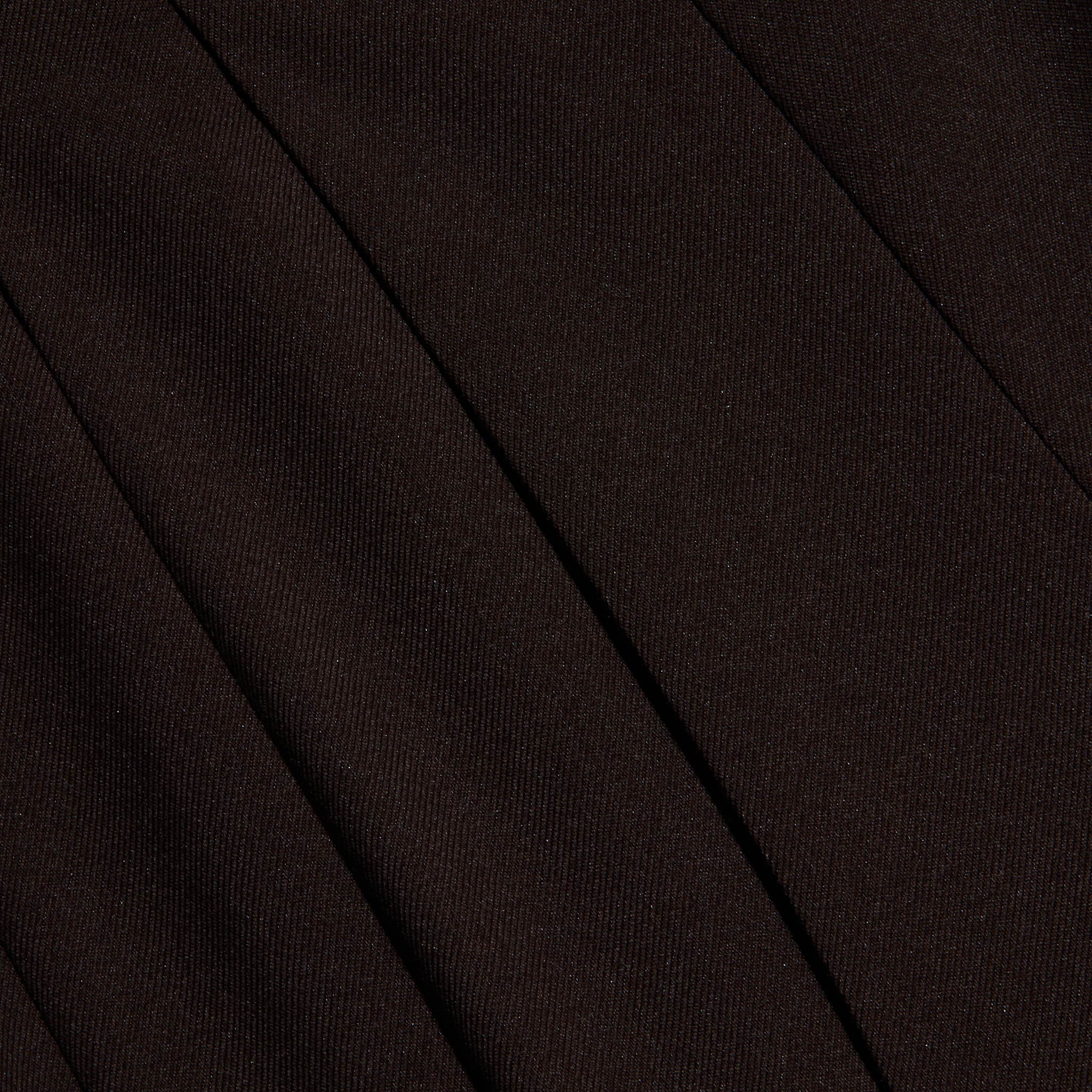 Close-up of black twill fabric with visible diagonal ribbing and seams, suggesting tailored clothing such as trousers or a skirt. The texture and folds create subtle shadows.