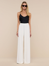A woman in sunglasses wears a black sleeveless top and the Nova Pleated Wide-Leg Pant in ivory, standing against a plain white background.