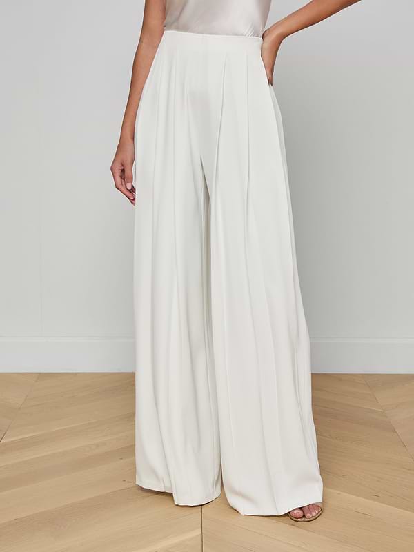 A person wearing the Nova Pleated Wide-Leg Pant in ivory stands against a plain white background. Only the lower part of the body is visible.