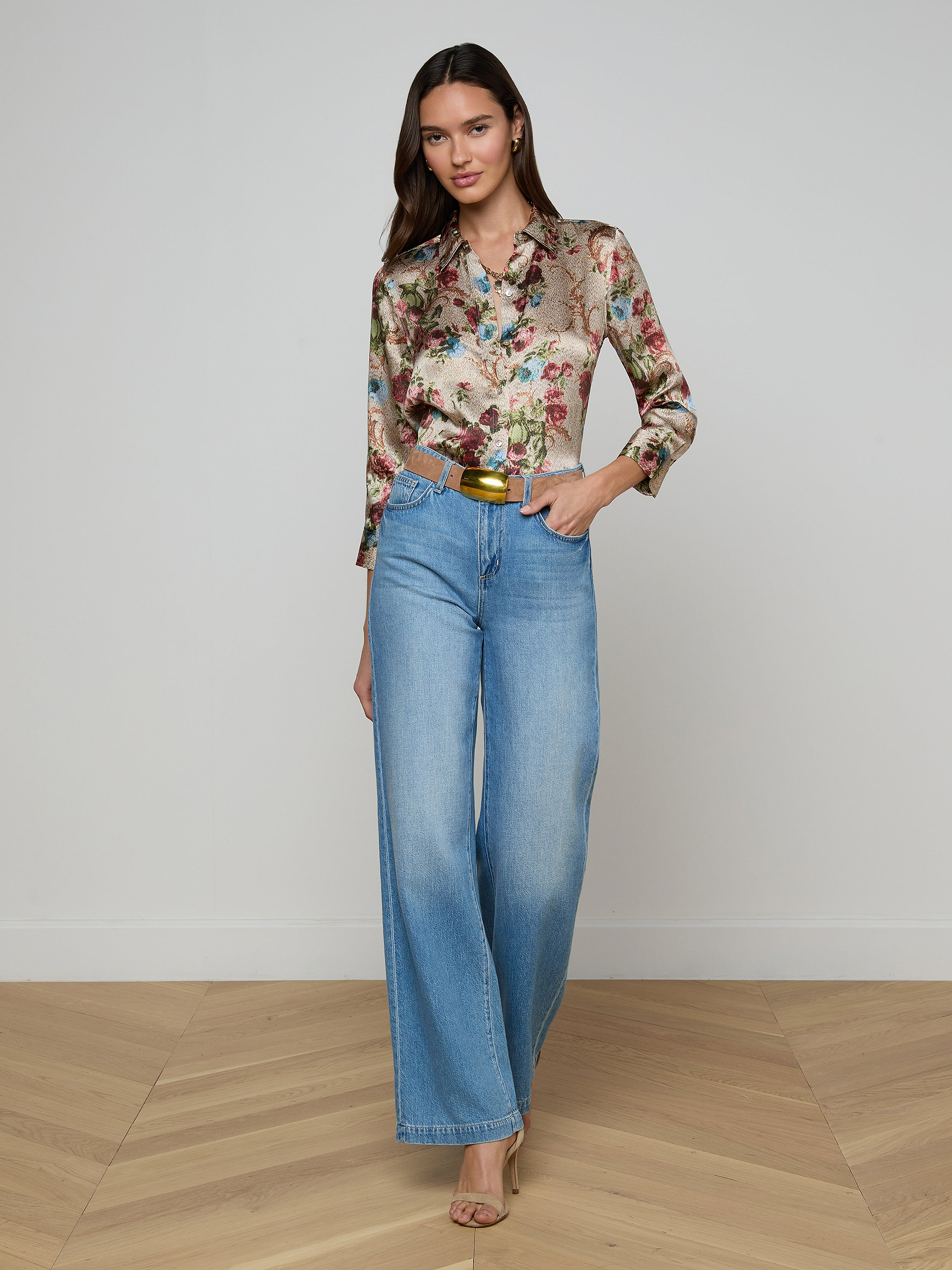 A woman wearing a floral long-sleeve blouse, the Scottie Wide-Leg Jean in a light wash with a contoured waistband, and beige heels stands against a plain white background.