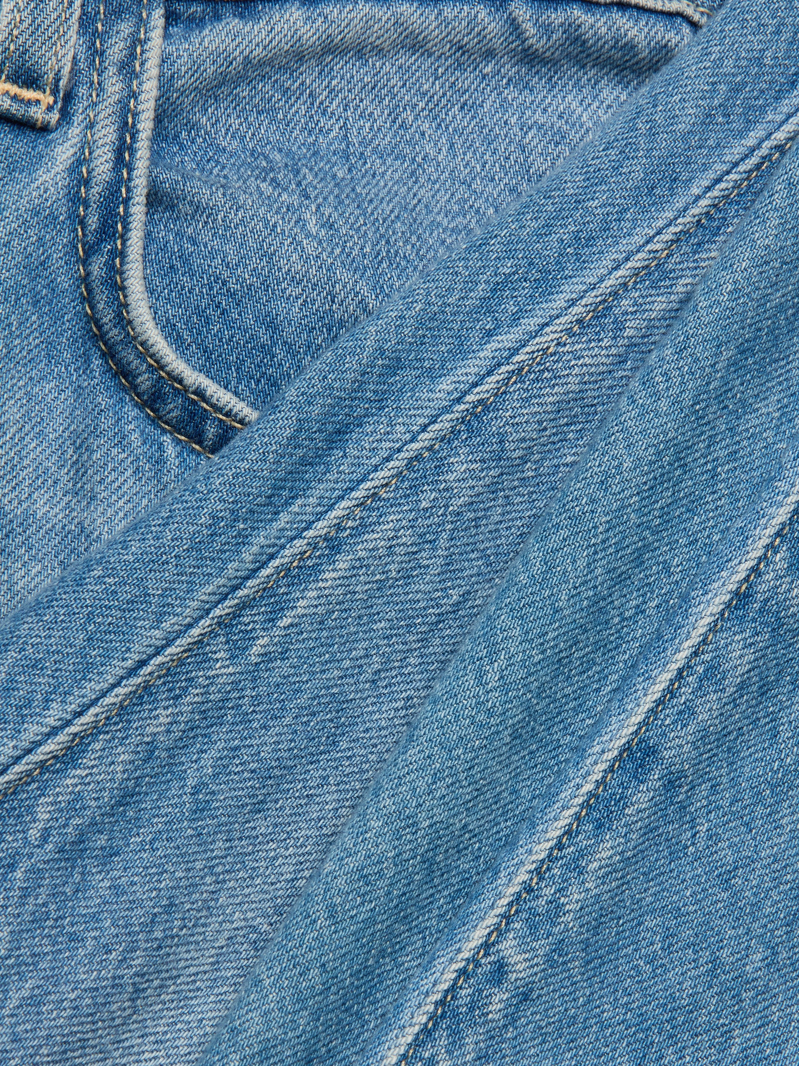 Close-up of the Scottie Wide-Leg Jean in blue denim, highlighting the stitching and a pocket, with another piece of light wash Scottie Wide-Leg Jean fabric laid diagonally across the image.