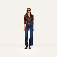 Woman wearing sunglasses, a dark brown satin button-up shirt, the Scottie Wide-Leg Jean in super stretch denim, a brown belt, and brown ankle boots stands against a plain white background.