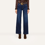 A person wearing high-waisted, wide-leg blue jeans and a brown long-sleeve blouse styled with a brown belt featuring a gold buckle and brown heeled boots stands confidently against a white background.