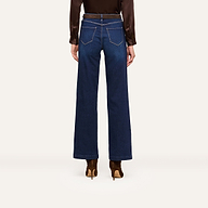 Person standing against a white background, shown from the back, wearing wide-leg dark blue jeans, a brown long-sleeve blouse, and stylish brown heeled boots.