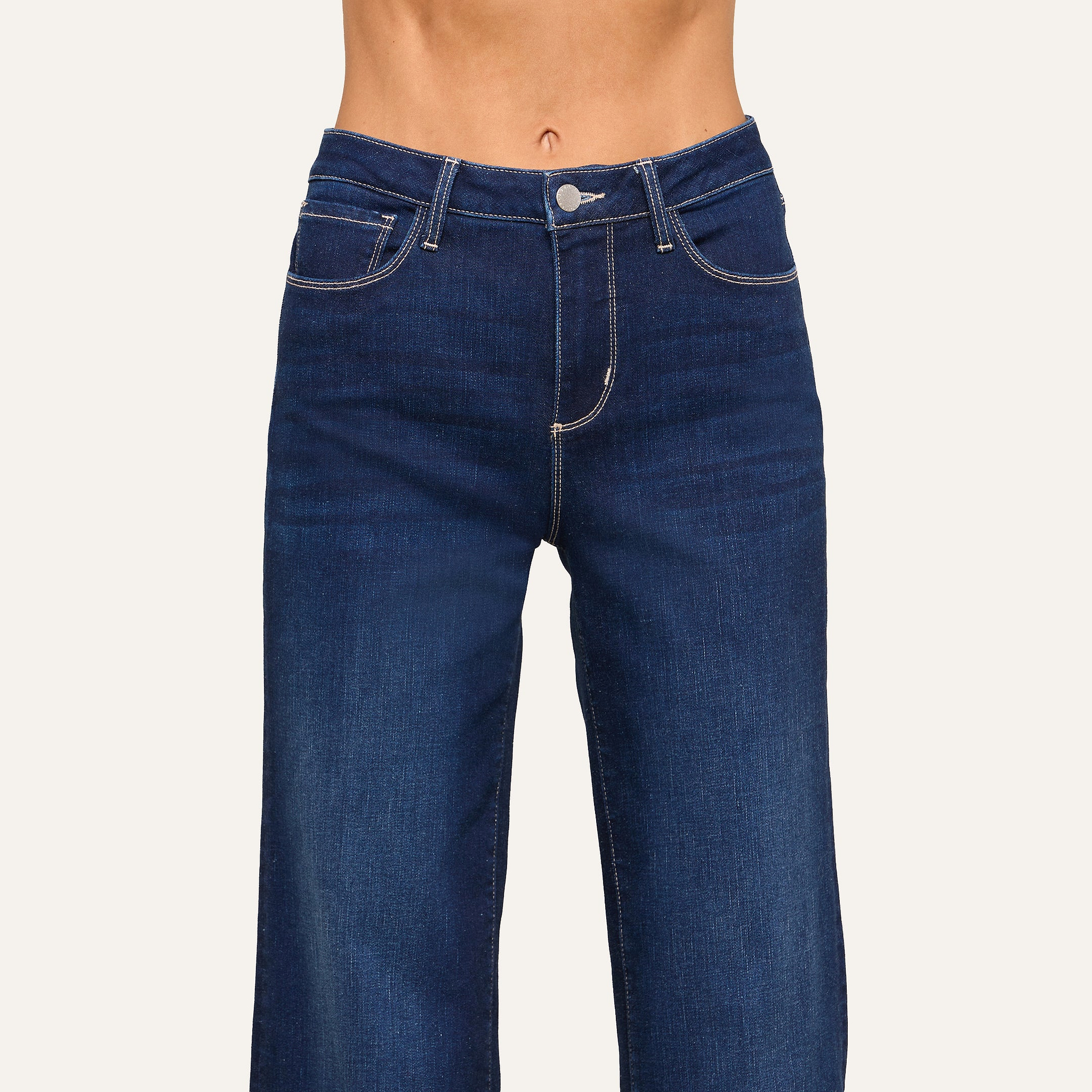 A person wearing high-waisted, dark blue jeans with white stitching is shown from waist to mid-thigh against a plain background.