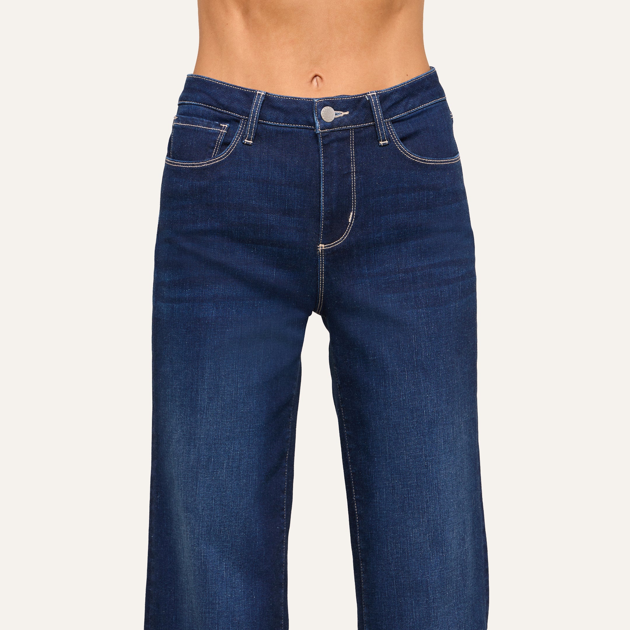 A person wearing high-waisted, dark blue jeans with white stitching is shown from waist to mid-thigh against a plain background.