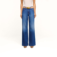 A person wearing a white sleeveless top, the Scottie Wide-Leg Jean in an indigo wash, a brown belt with a gold buckle, and brown shoes stands against a plain white background.