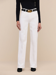Wearing the Scottie Wide-Leg Jean in white, a person stands against a plain light background, styled with a black sleeveless top, a white belt with a gold buckle, and black pointed-toe shoes.