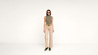 Woman wearing sunglasses, a sleeveless olive top, beige high-waisted wide-leg pants, a brown belt, and green heeled boots stands against a plain white background.