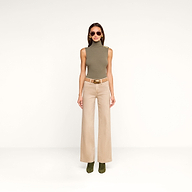 A woman in a sleeveless, olive-green turtleneck top, the Scottie Coated Wide-Leg Jean, green boots, and sunglasses stands against a plain white background.