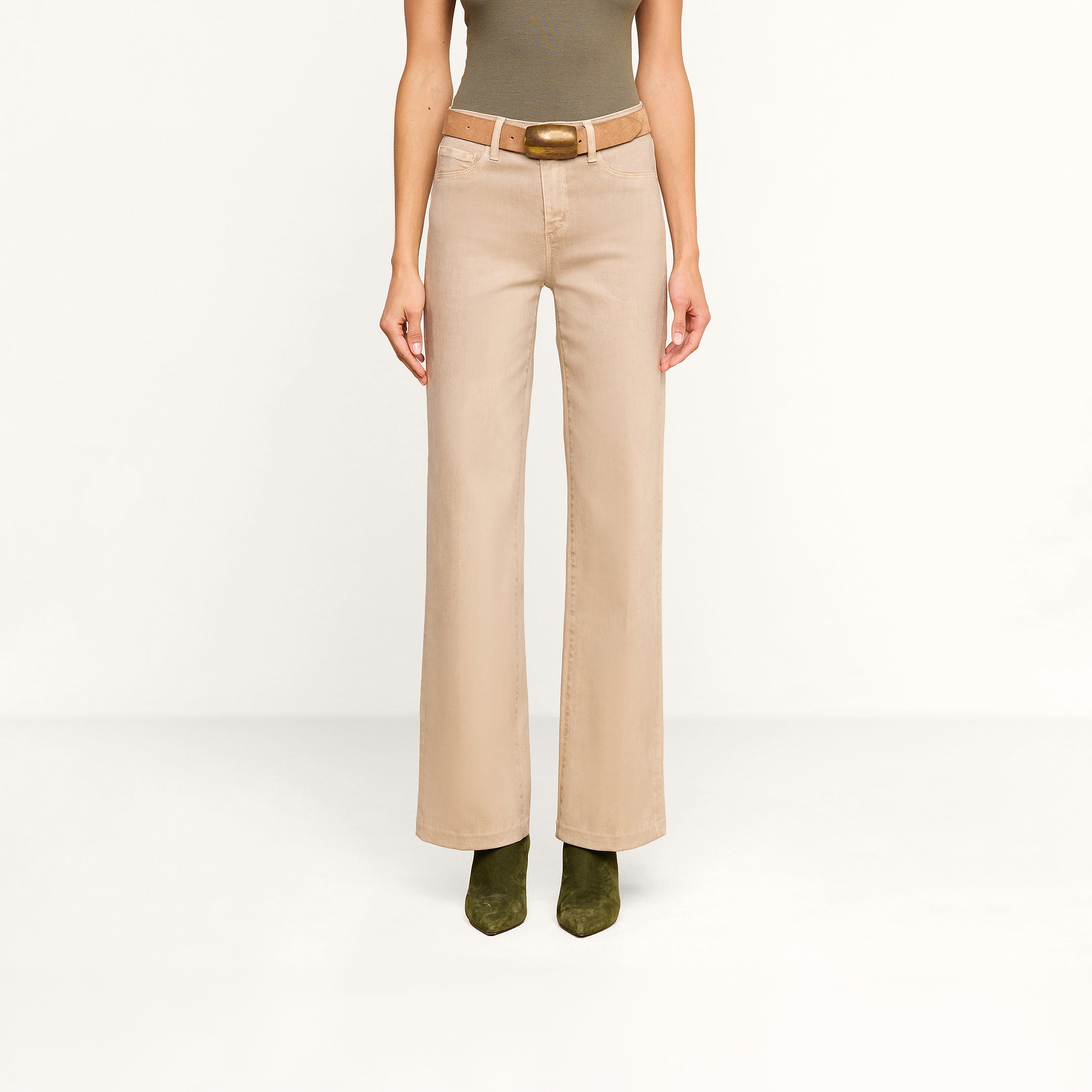 A person wearing the Scottie Coated Wide-Leg Jean in beige, styled with a brown belt, paired with a fitted olive sleeveless top and olive green boots, stands against a plain white background.