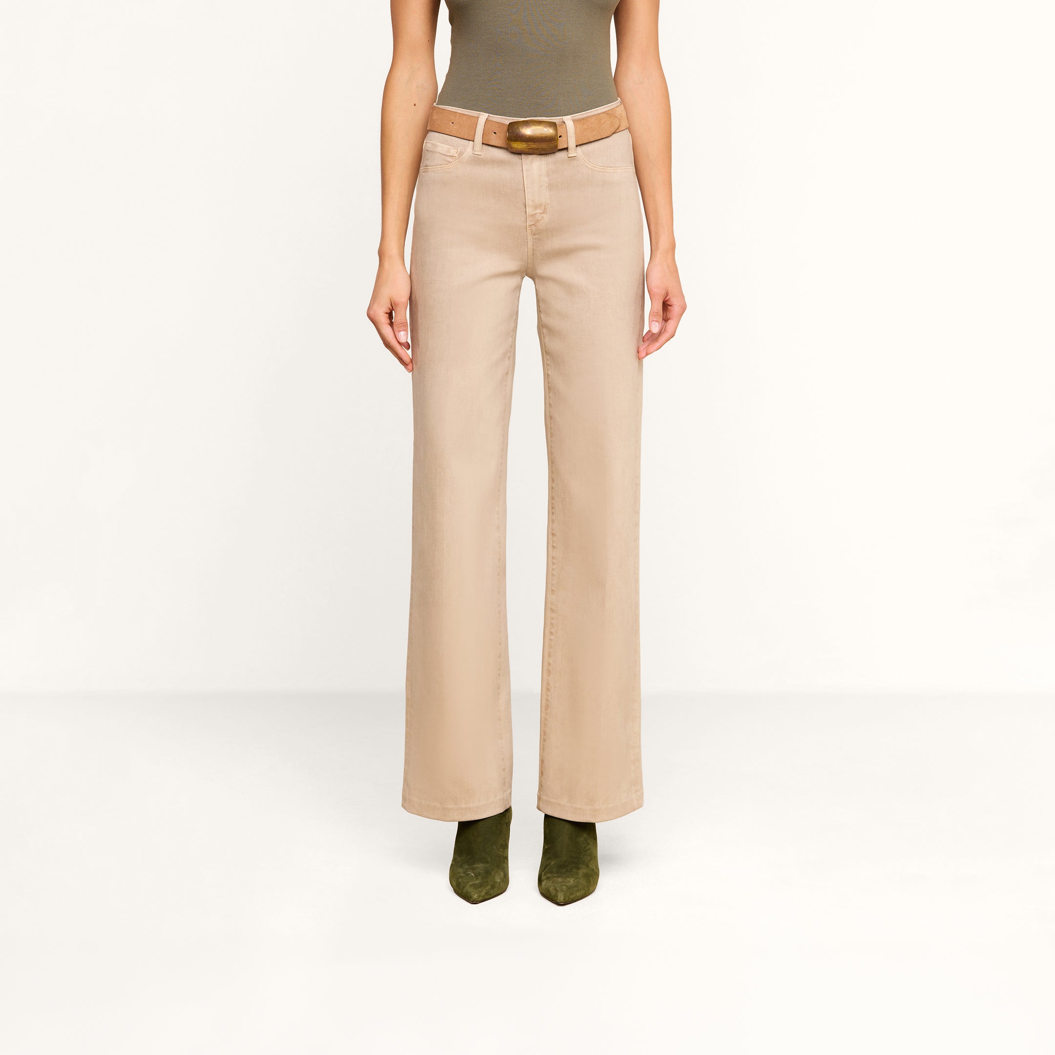 A person wearing the Scottie Coated Wide-Leg Jean in beige, styled with a brown belt, paired with a fitted olive sleeveless top and olive green boots, stands against a plain white background.