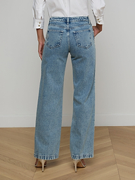 A person wearing a white long-sleeve shirt, beige high heels, and the Scottie Embellished Wide-Leg Jean in blue all-cotton denim is standing with their back to the camera against a plain light background.