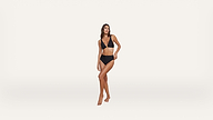 A woman poses against a plain white background, wearing a black bikini with a V-neck top and high-cut bottoms.