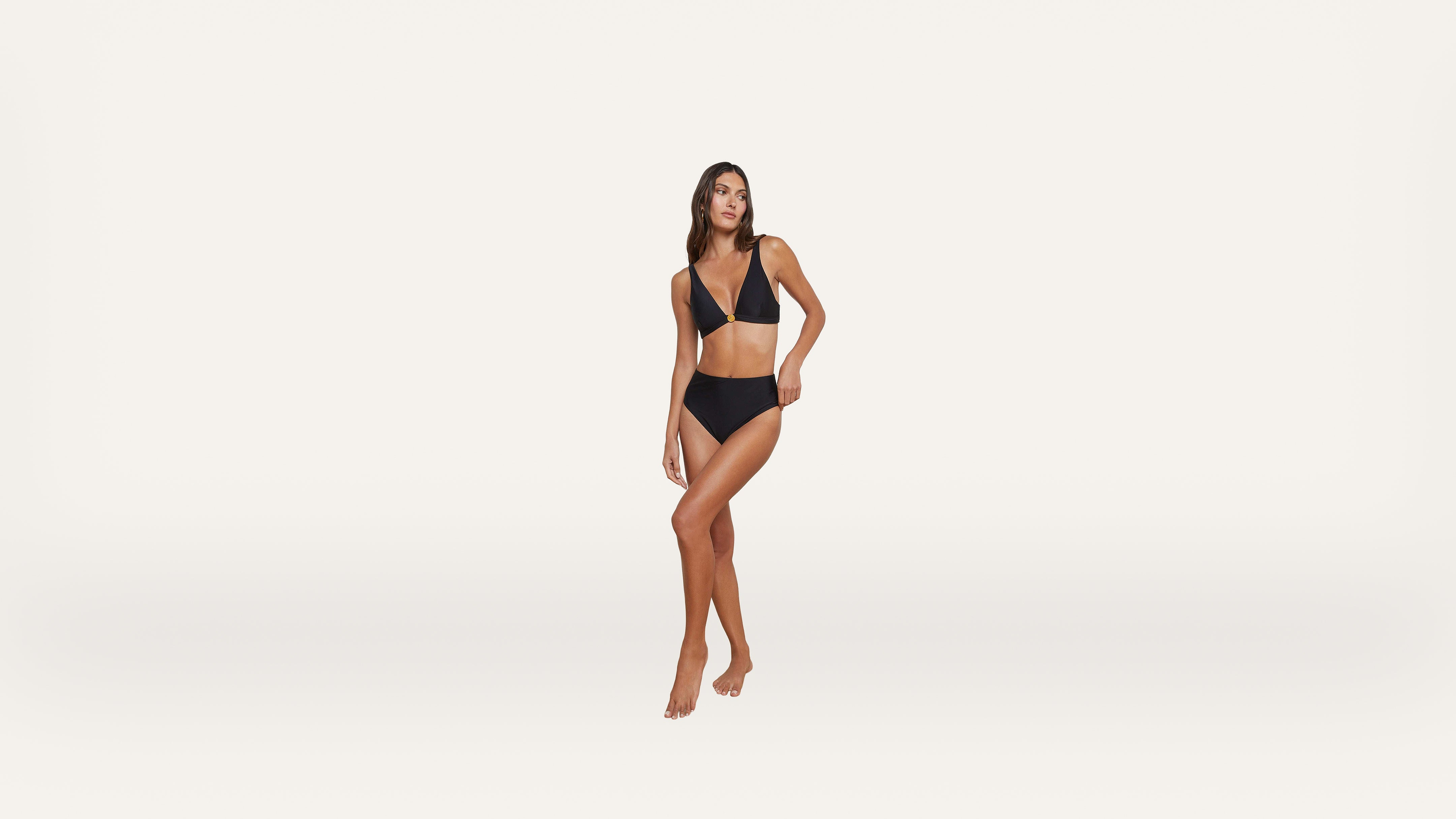 A woman poses against a plain white background, wearing a black bikini with a V-neck top and high-cut bottoms.