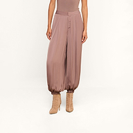 A person wearing the Palmer Satin Pant—high rise, loose-fitting mauve balloon trousers with gathered ankles—paired with matching heeled boots, shown from shoulders down against a plain background.