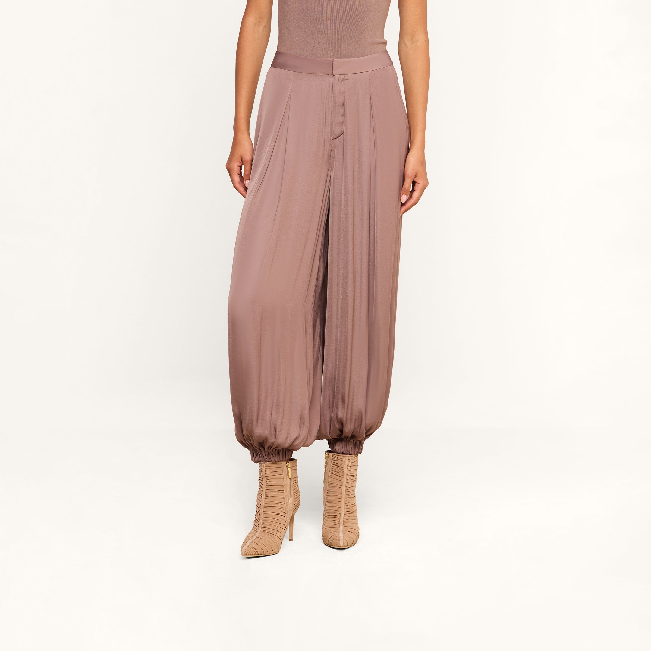 A person wearing the Palmer Satin Pant—high rise, loose-fitting mauve balloon trousers with gathered ankles—paired with matching heeled boots, shown from shoulders down against a plain background.