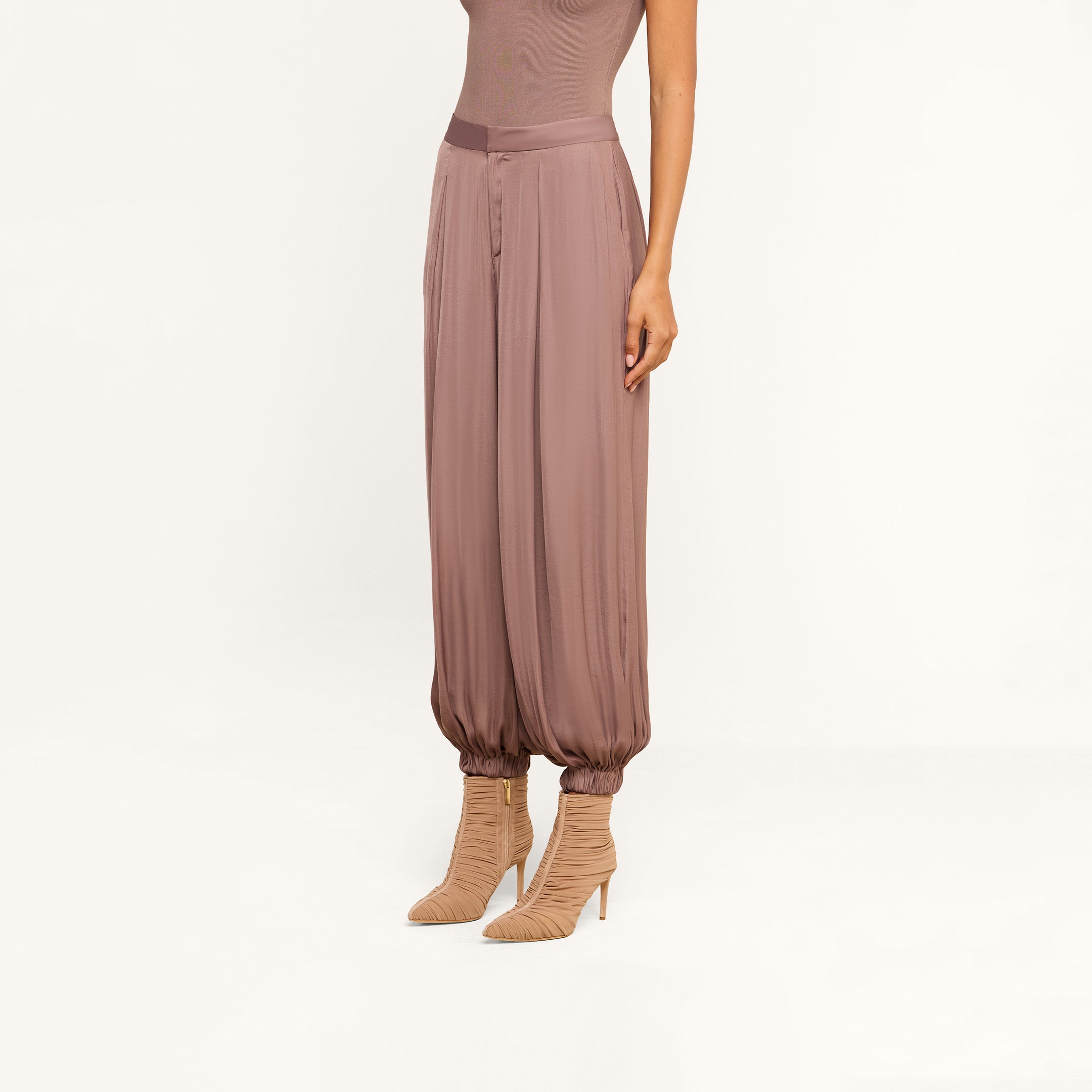 A person wearing the Palmer Satin Pant in a loose, mauve-colored satin style with gathered ankles and beige high-heeled boots, shown from the neck down against a plain background.