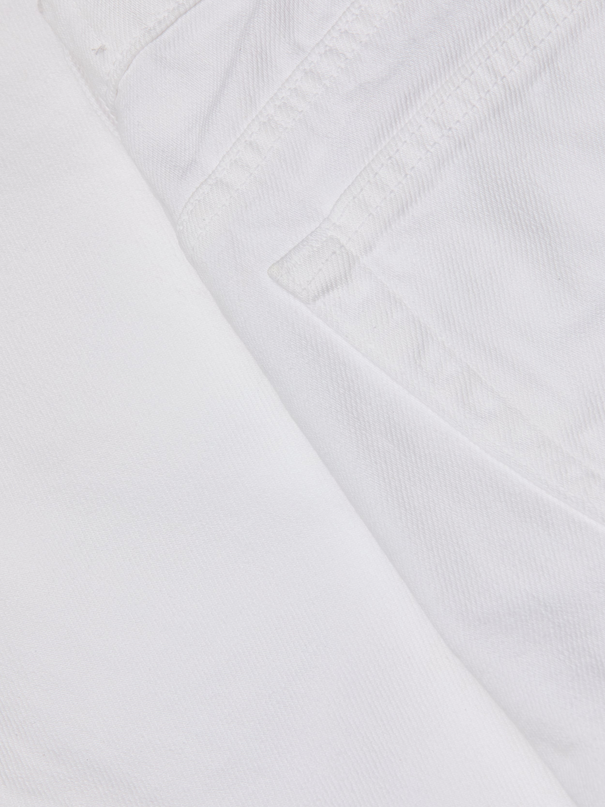 Close-up of the Krista Tapered Jean in white denim, focusing on the pocket and stitched seam details, with textured stretch denim fabric visible. The image highlights the weave and structure characteristic of these high-rise tapered leg jeans.
