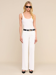 Eine Frau mit schwarzer Sonnenbrille, einem weißen Trägertop und einer schicken „Joanne Low-Rise Wide-Leg Jeans“ mit schwarzem Gürtel und schwarzen Pumps steht vor einem schlichten beigen Hintergrund.