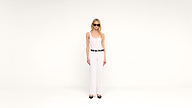 A person with long blonde hair wears a white tank top, white pants, a black belt, black shoes, and sunglasses, standing against a plain white background.