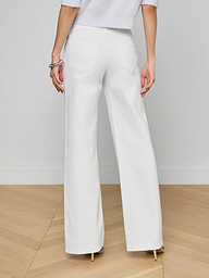 Person standing facing away, wearing Joanne Low-Rise Wide-Leg Jeans with a black belt and black high heels, against a plain white background. Only the lower half of the body is visible.