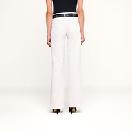 Eine Person ist von hinten vor einem beigen Hintergrund zu sehen. Sie trägt eine weiße „Joanne Low-Rise Wide-Leg Jeans“, einen schwarzen Gürtel und schwarze Schuhe mit Absatz.