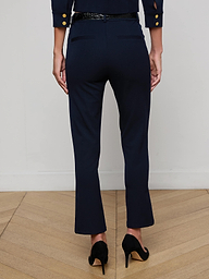 A person stands with their back to the camera, wearing the Ketra Bootcut Trouser in midnight navy and a matching blazer with gold buttons, both crafted from stretch suit fabric, paired with black high heels against a plain white background.