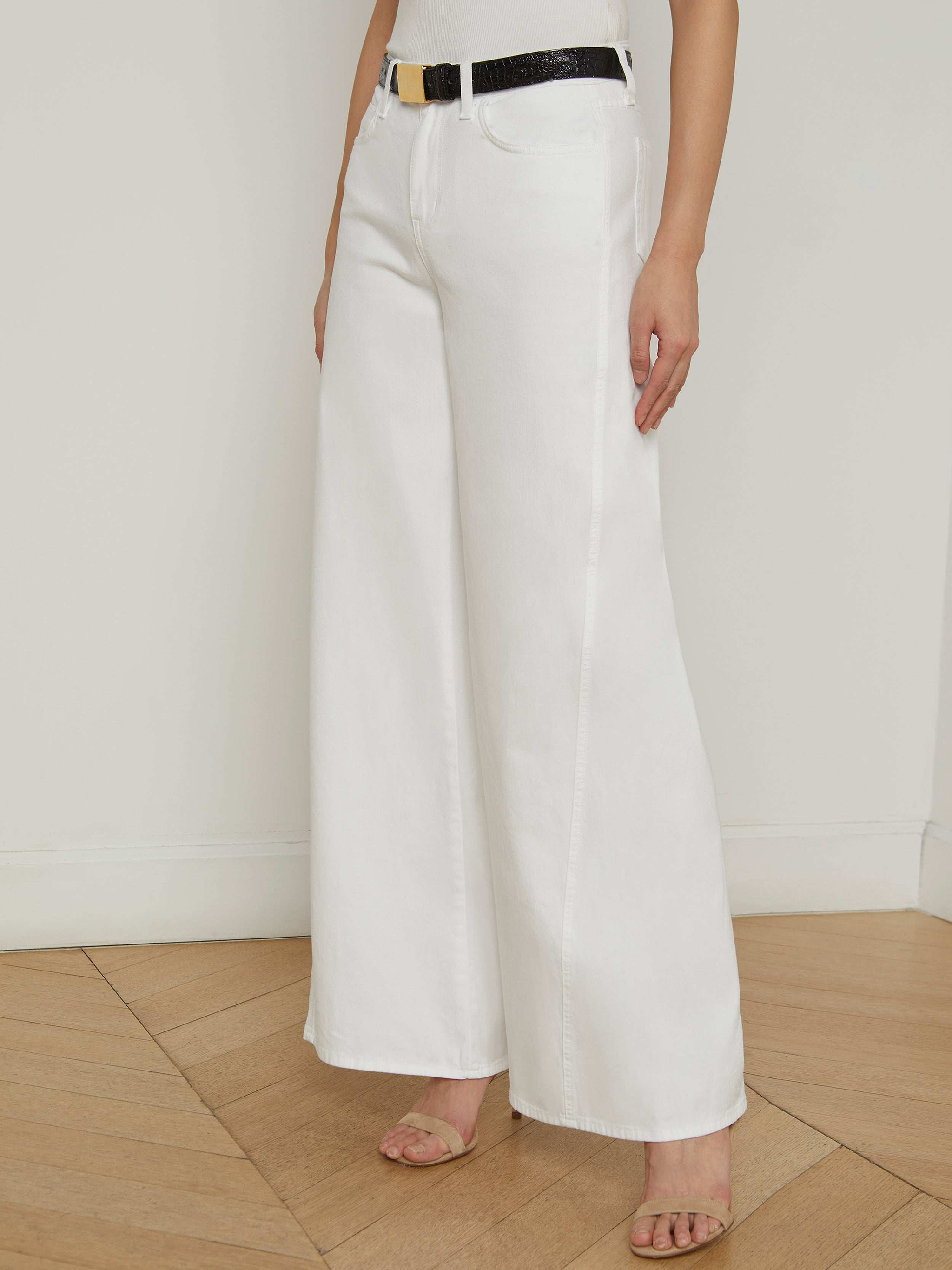 A person wearing the Beau Wide-Leg Jean in white, styled with a black belt and open-toe heels, stands against a plain, light background.